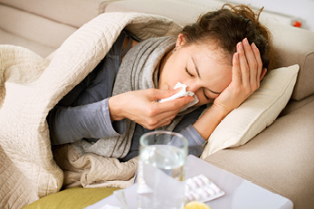 woman on couch blowing nose into tissue woman on couch blowing nose into tissue